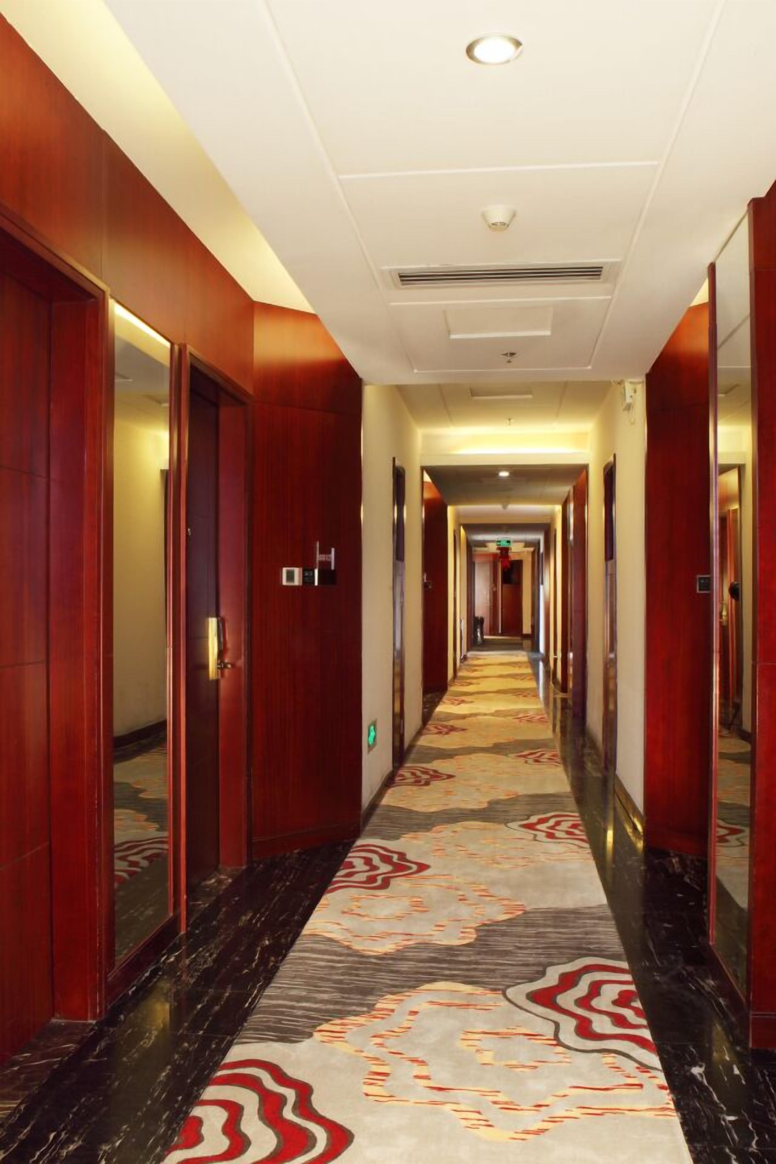 A hotel hallway with wooden doors, a patterned carpet, and a ceiling with recessed lighting.