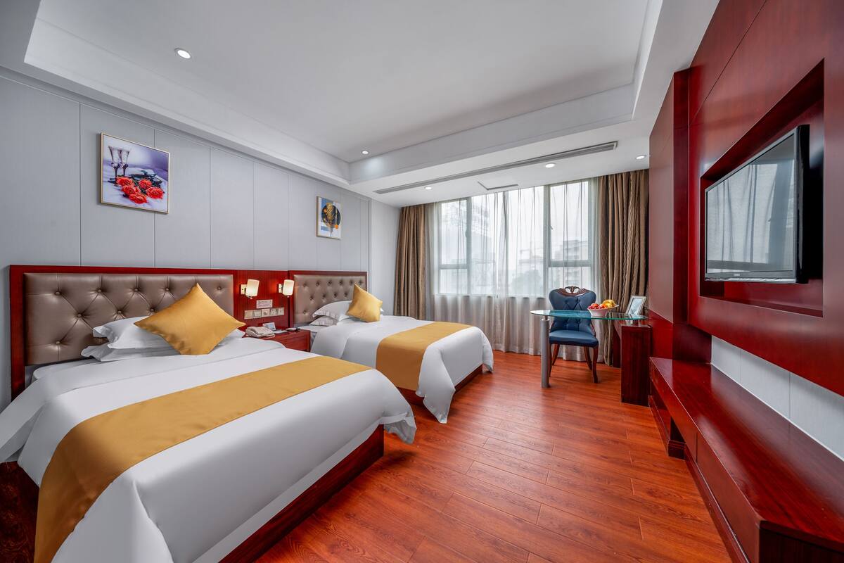 Een hotelkamer met twee bedden, een televisie, een bureau en een raam met gordijnen.