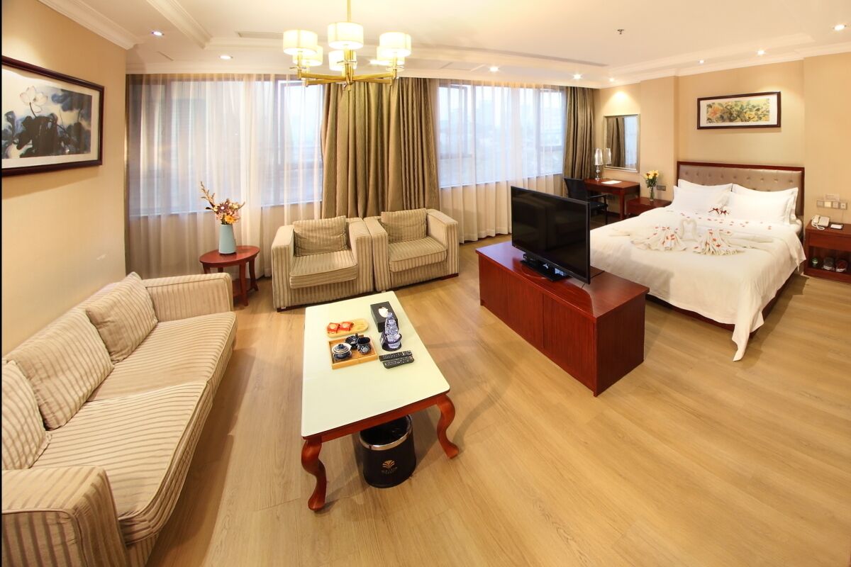 A hotel room with a bed, a sofa, a TV, a coffee table, and a desk.