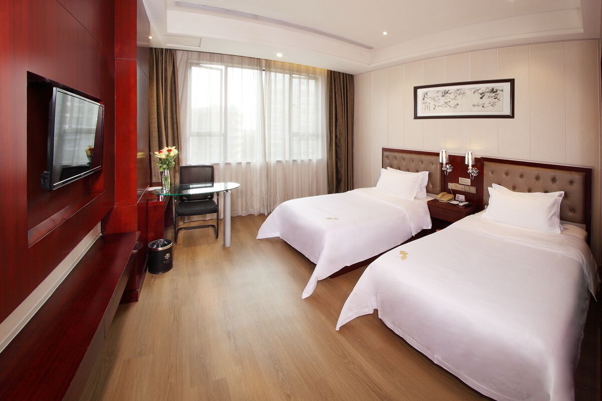 A hotel room with two beds, a TV, a small table with a chair, and a window with curtains.