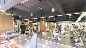 Uma academia com diversos equipamentos de exercício, espelhos e um espaço amplo.