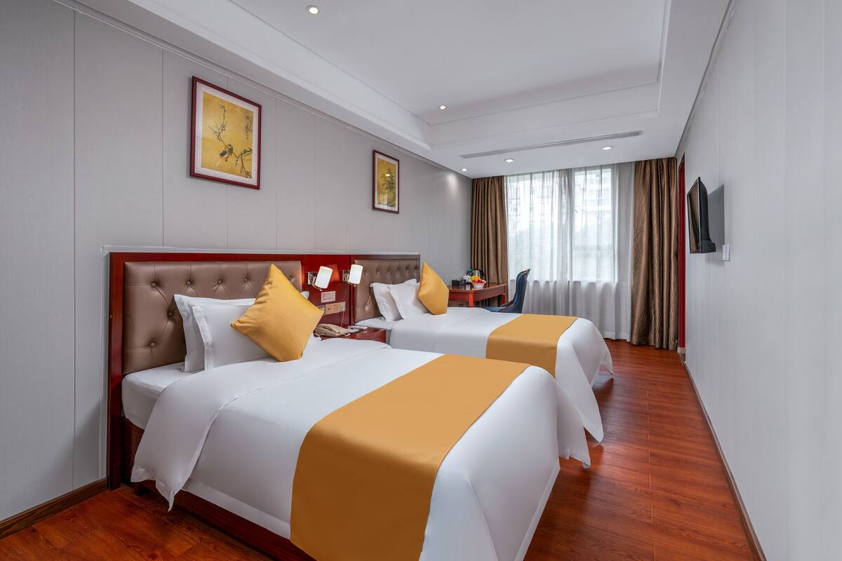 Een hotelkamer met twee bedden, een houten vloer, een televisie en een raam met gordijnen.