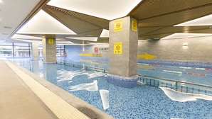 Piscina interior com paredes azulejadas e chão azul, exibindo placas de segurança e setas indicativas.