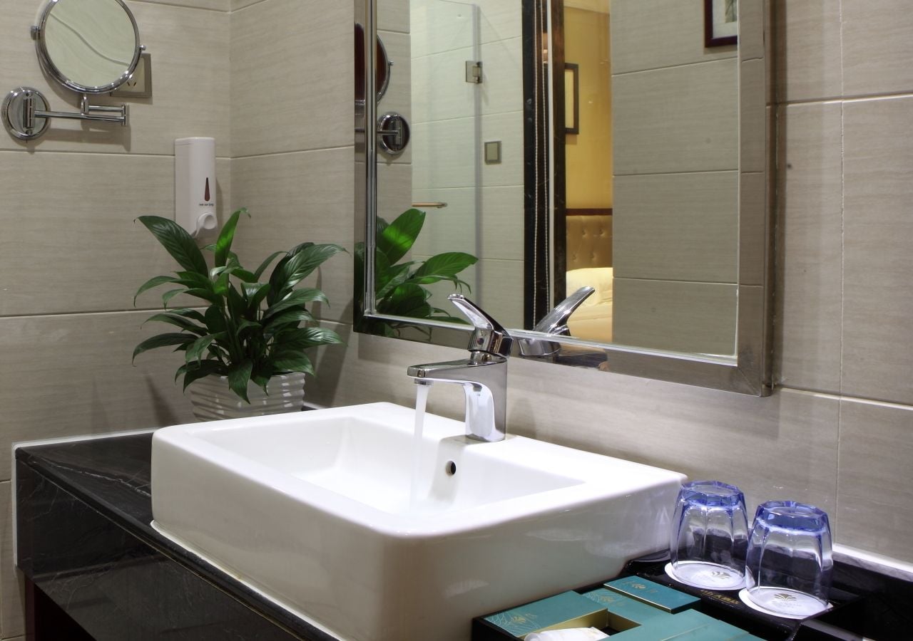 A bathroom with a white sink, two mirrors, a potted plant, and a towel rack.