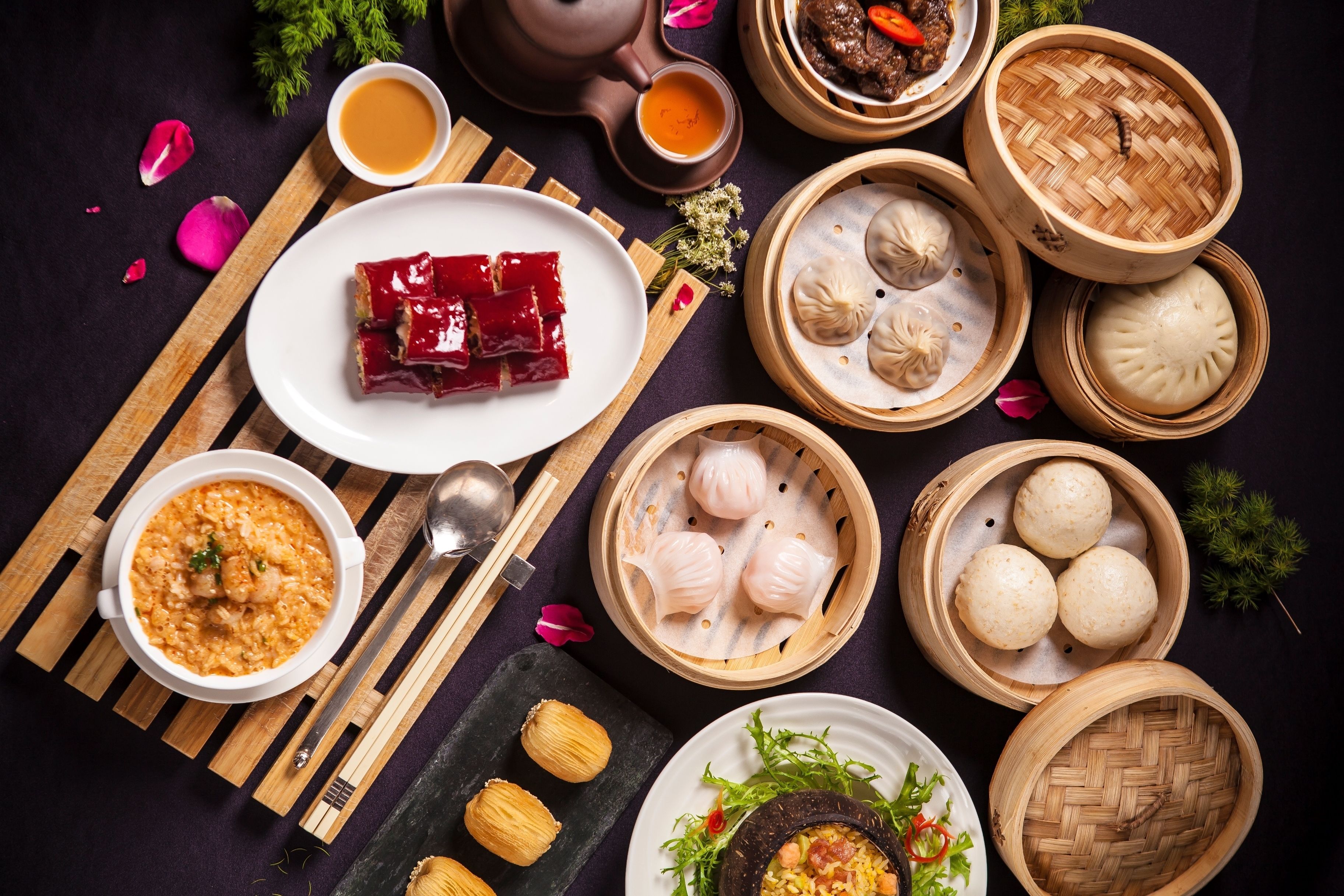 A variety of Chinese dishes including dim sum, a bowl of rice, and a plate of red meat.