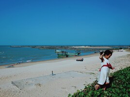 Una playa con barcos, un sendero de hormigón y una persona vestida de blanco.