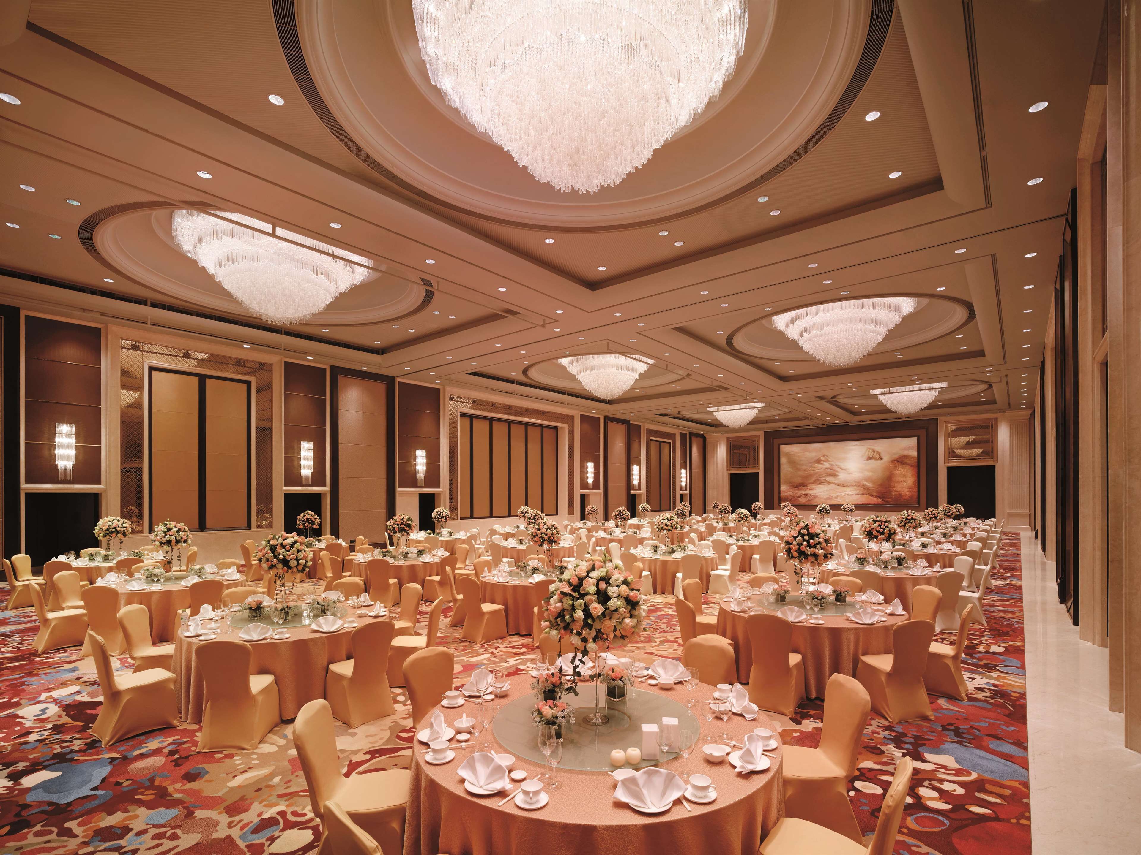 A large banquet hall with round tables, chairs, and chandeliers.