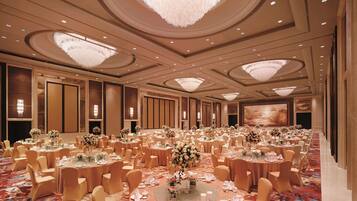 A large banquet hall with round tables, chairs, and chandeliers.