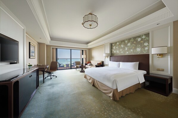 A hotel room with a large bed, a desk with a television, a chair, a nightstand, and a view of the outdoors. - Grand Hotel Haikou (Managed by Accor) (Haikou)