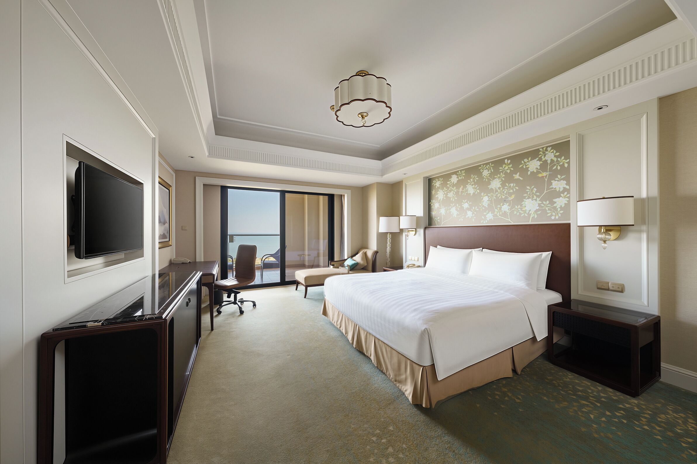 A hotel room with a bed, a desk, a TV, a chair, and a large window.