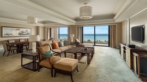 Amplia sala de estar con un gran ventanal que ofrece vistas al océano, una zona de estar confortable con sofá y sillones, una mesa de centro y un televisor en la pared.