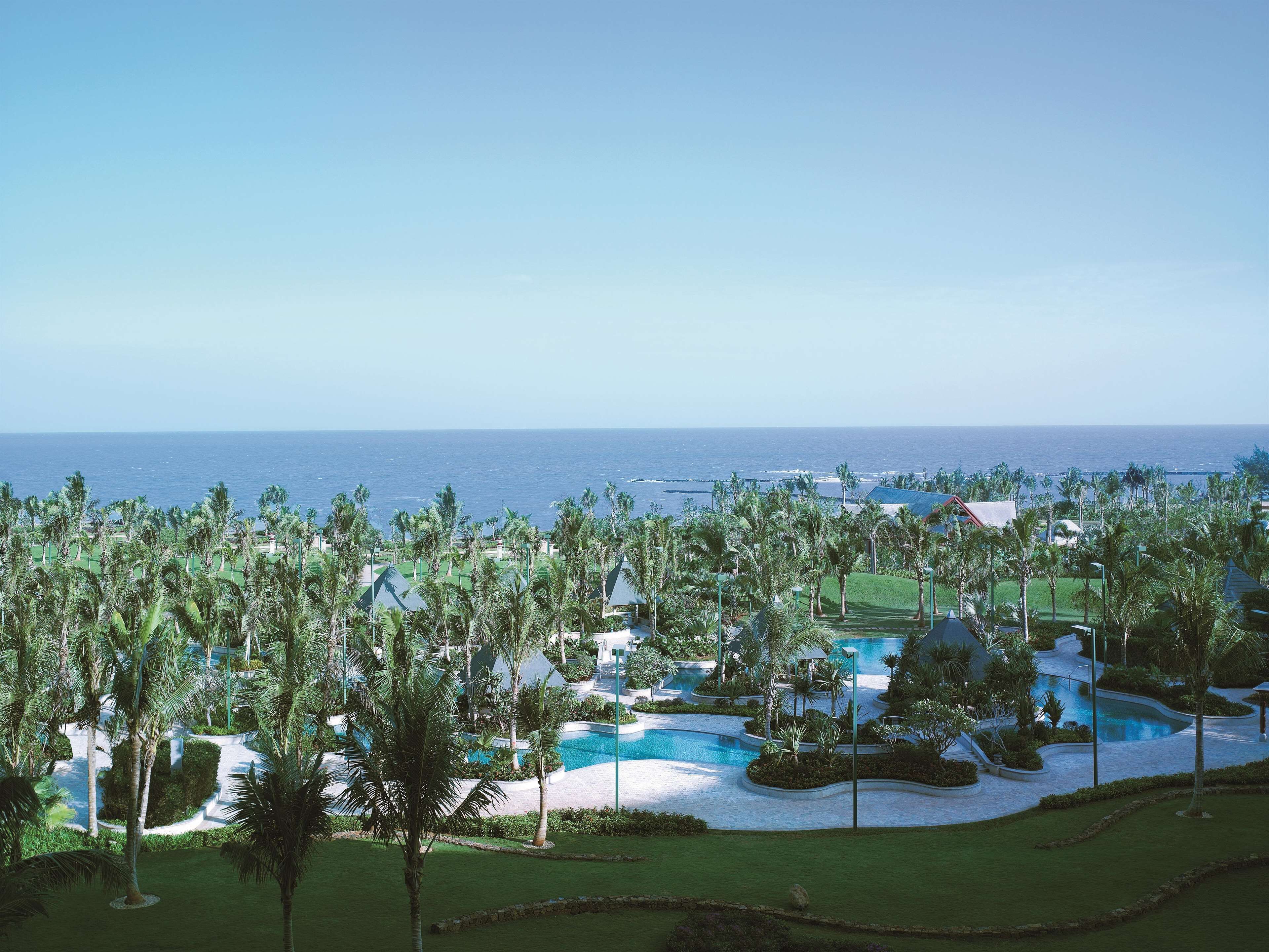 A resort with a pool, palm trees, and a view of the ocean.