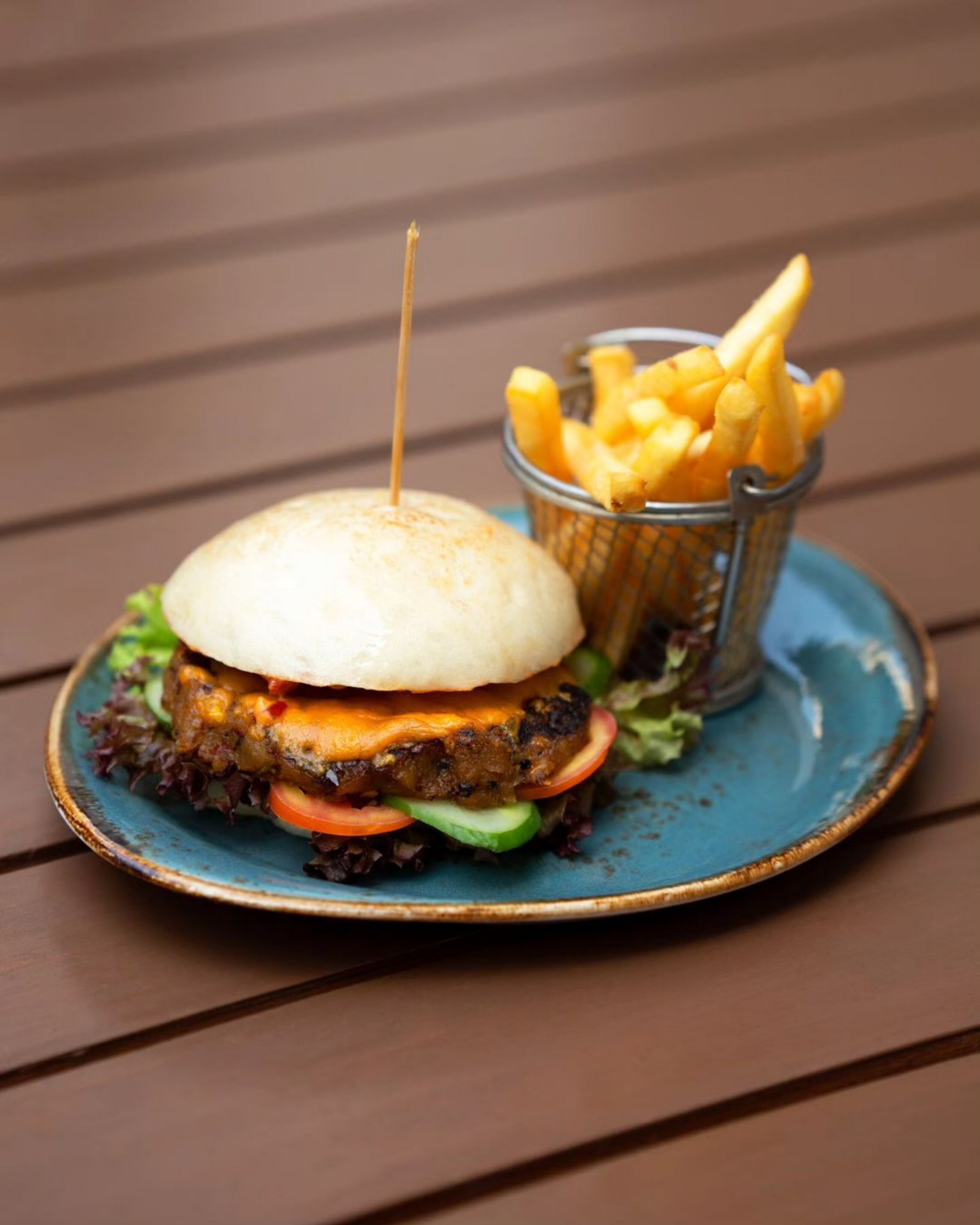 A burger with a toothpick, lettuce, tomato, and a bun, served with French fries on a blue plate.