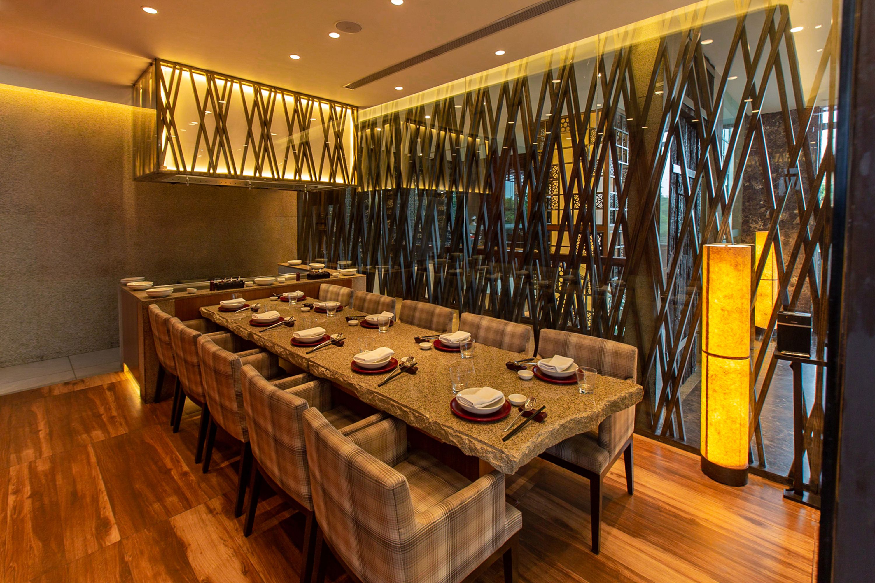 Una larga mesa de comedor con sillas, una lámpara moderna y un panel decorativo en la pared.