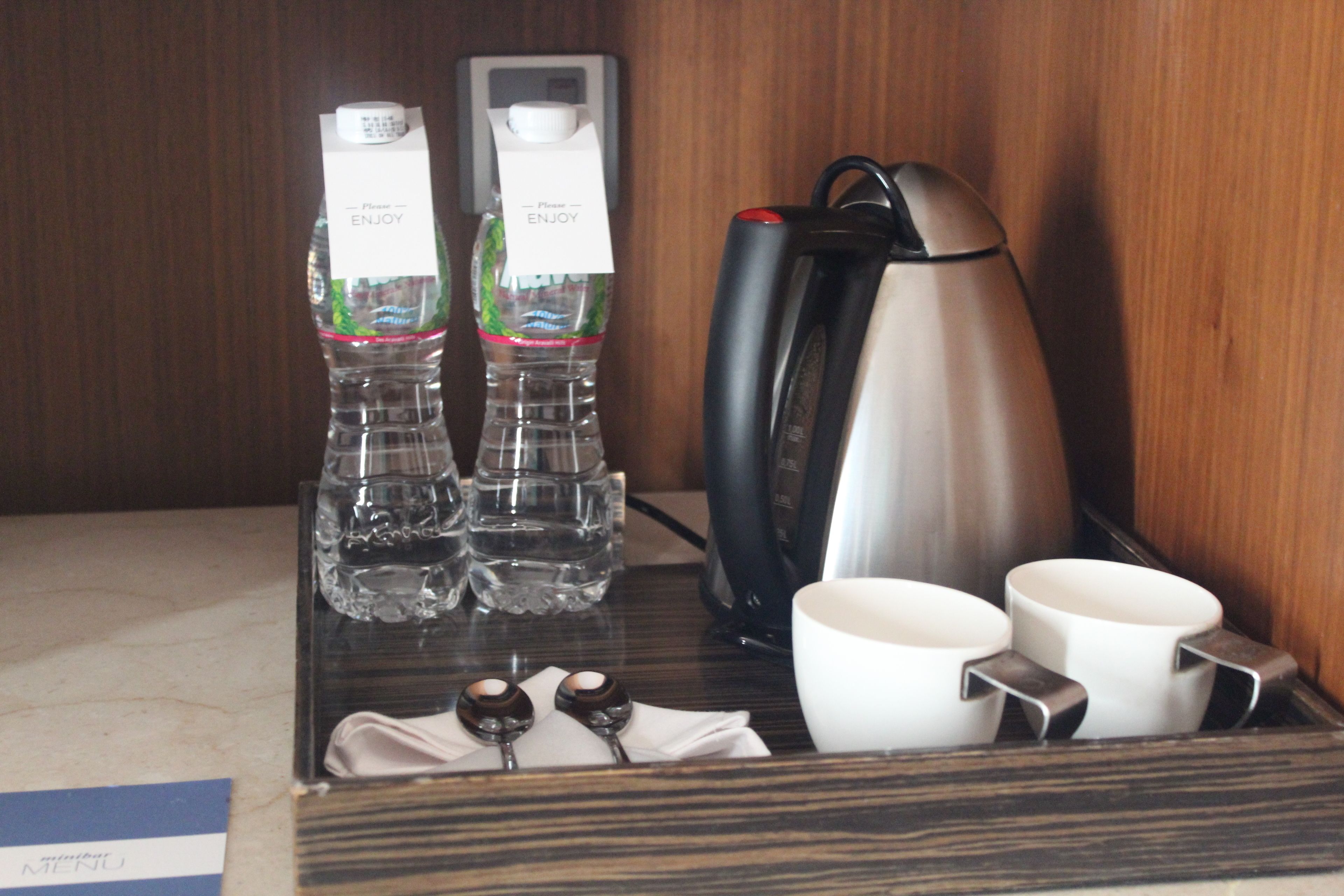 A hotel room's minibar with bottled water, a coffee maker, and white cups.