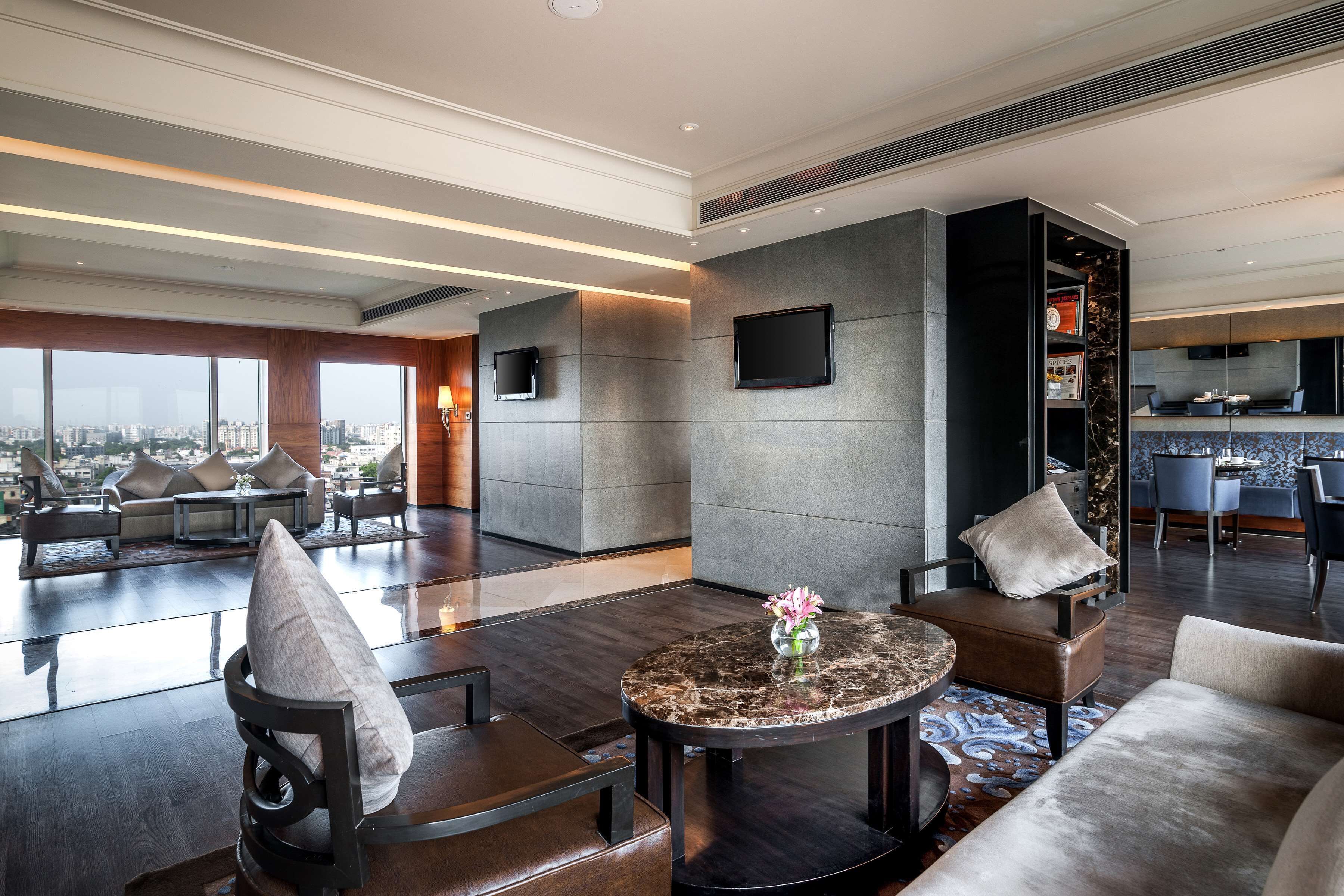Een moderne hotel lobby met een zithoek, een ronde tafel met een vaas en uitzicht op de stad.