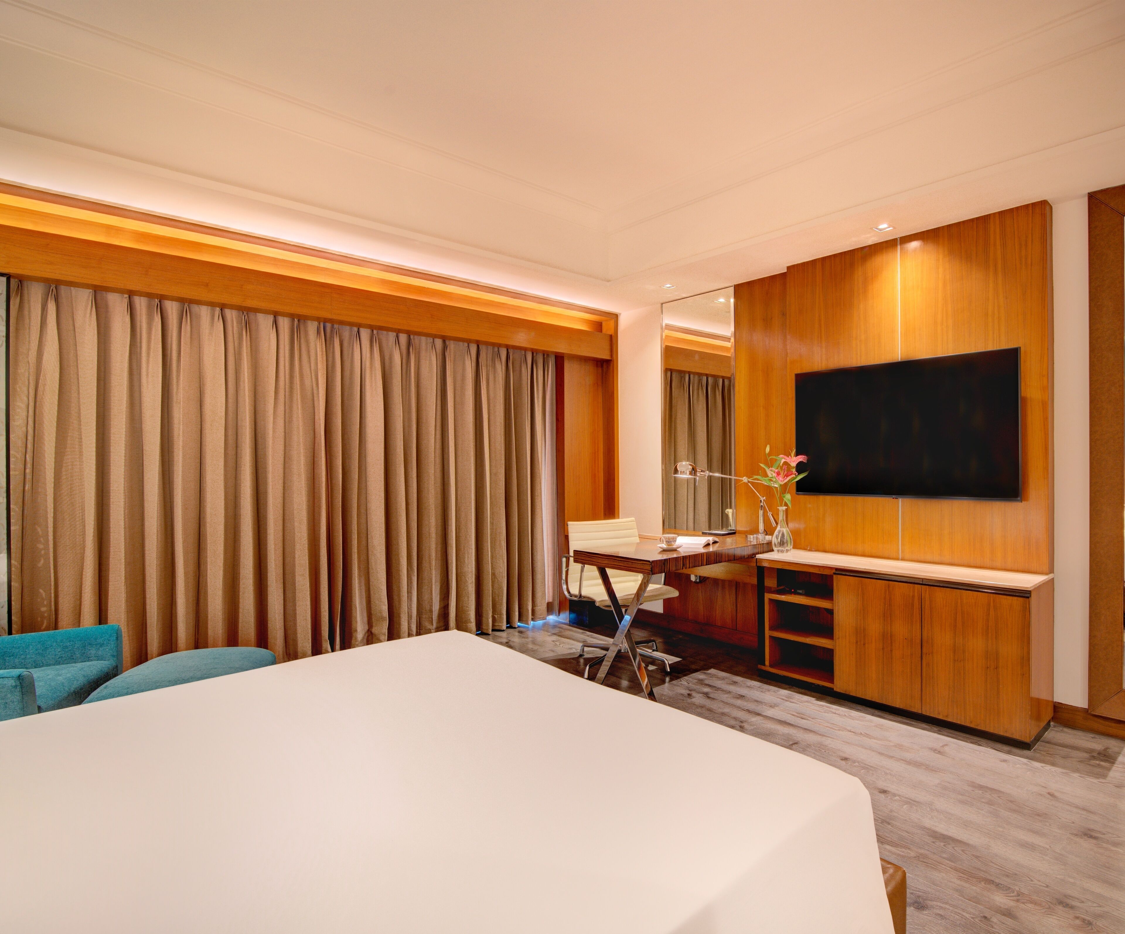 A hotel room with a large bed, a desk with a chair, a television mounted on the wall, and a window with curtains.