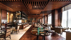 Un restaurante espacioso con vigas de madera en el techo, una barra larga con mostradores de comida y ventanas amplias que aportan luz natural.