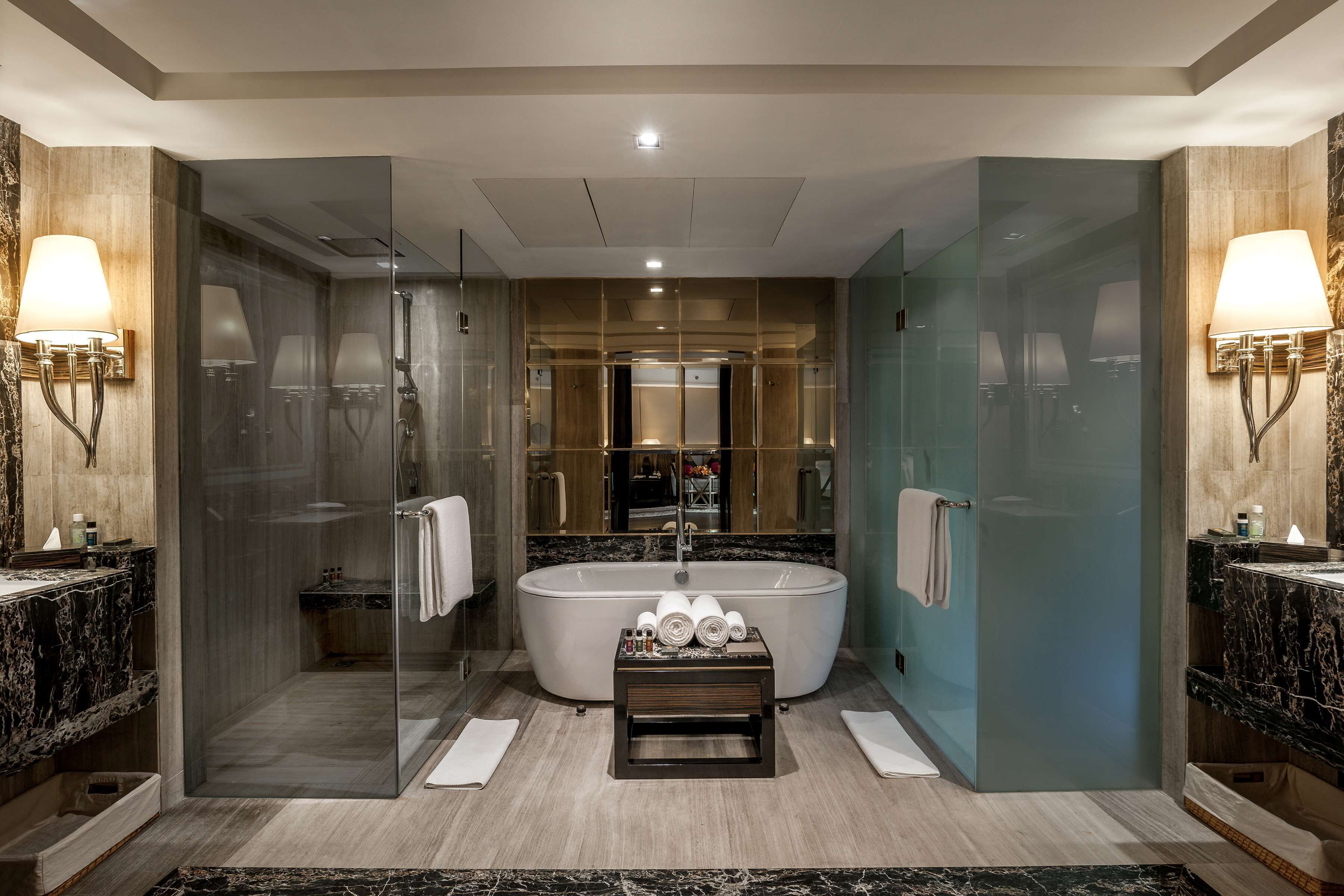 A modern bathroom with a freestanding bathtub, glass-enclosed shower, marble countertops, and wall-mounted lighting.