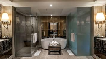 A modern bathroom with a freestanding bathtub, glass-enclosed shower, marble countertops, and wall-mounted lighting.