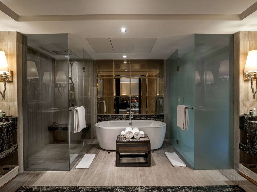 A modern bathroom with a freestanding bathtub, glass-enclosed shower, marble countertops, and wall-mounted lighting.