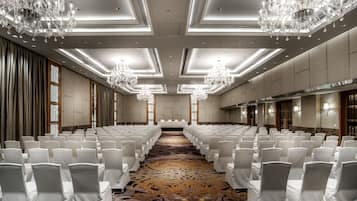 A conference room with rows of white chairs, chandeliers, and a carpeted floor.