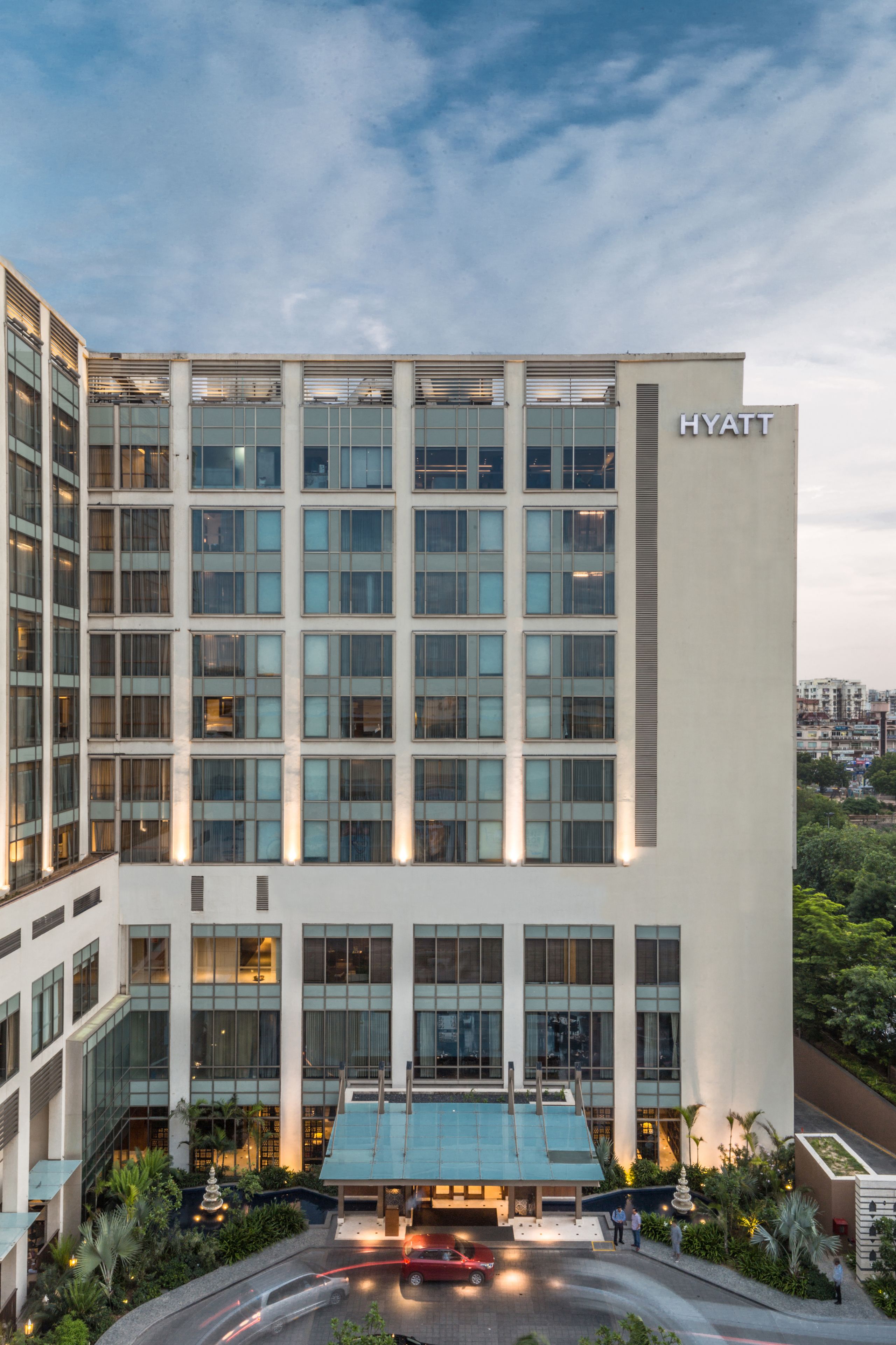 Ein modernes Hyatt Hotel mit einer großen Glasfassade, einem Pool auf dem Dach und einem begrünten Innenhof.