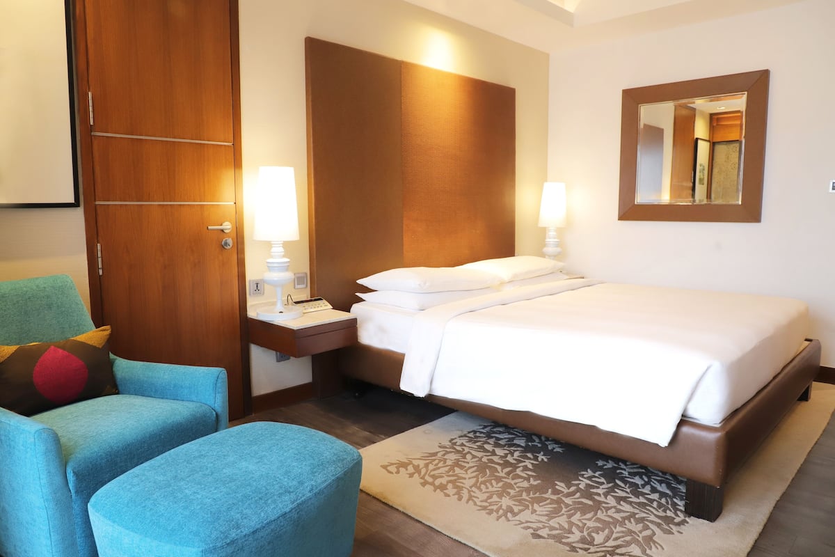 A hotel room with a bed, a nightstand, a lamp, a chair, and a large mirror on the wall.