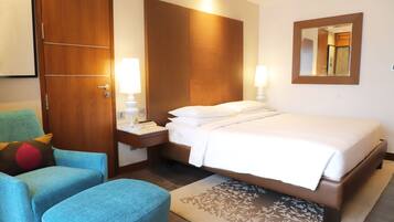 Habitación de hotel con cama, mesita de noche, lámpara, sillón y un espejo grande en la pared.