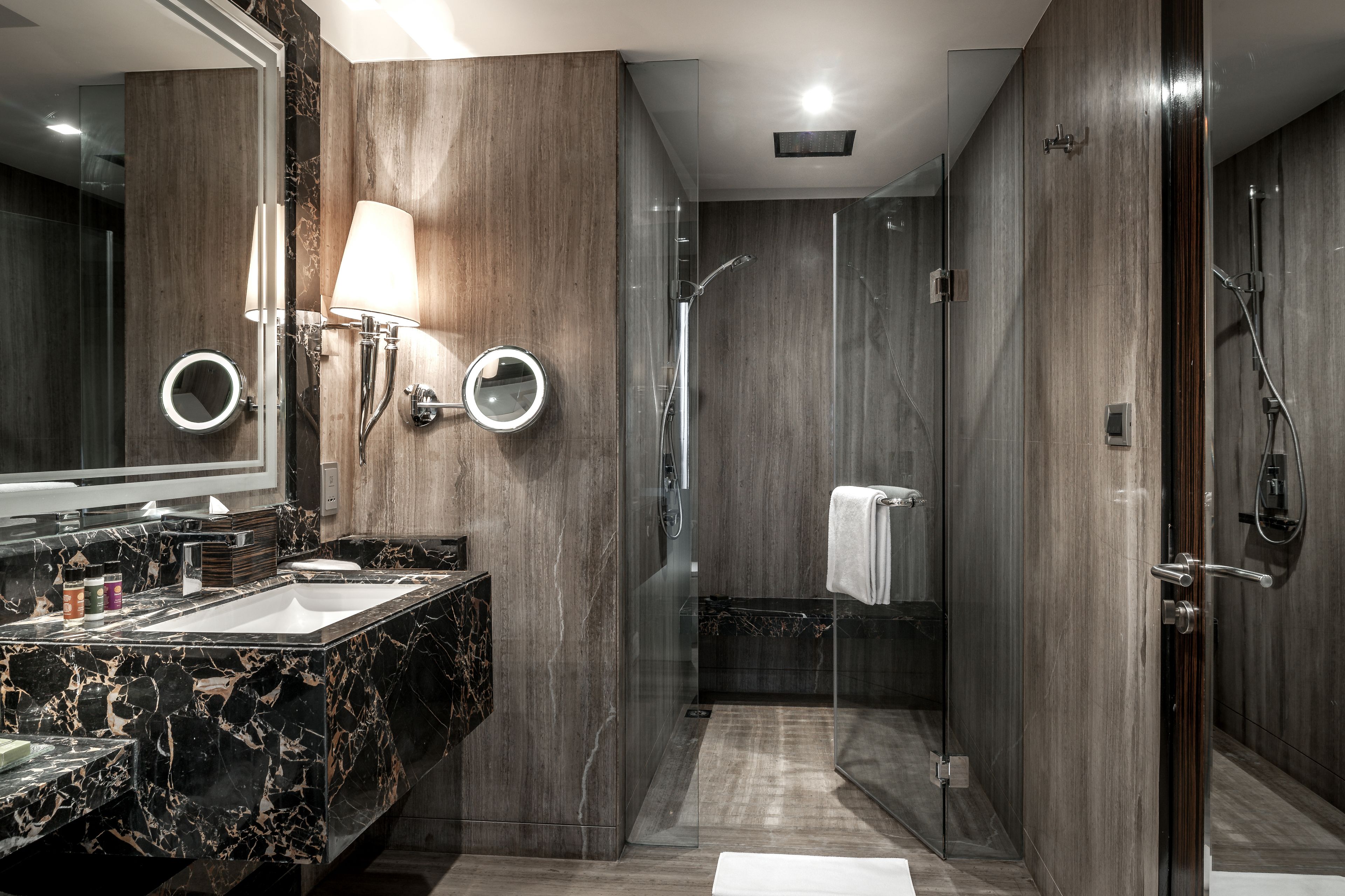 A modern bathroom with a marble sink, a large mirror, and a glass-enclosed shower area.