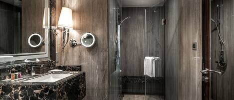 A modern bathroom with a marble sink, a large mirror, and a glass-enclosed shower area.