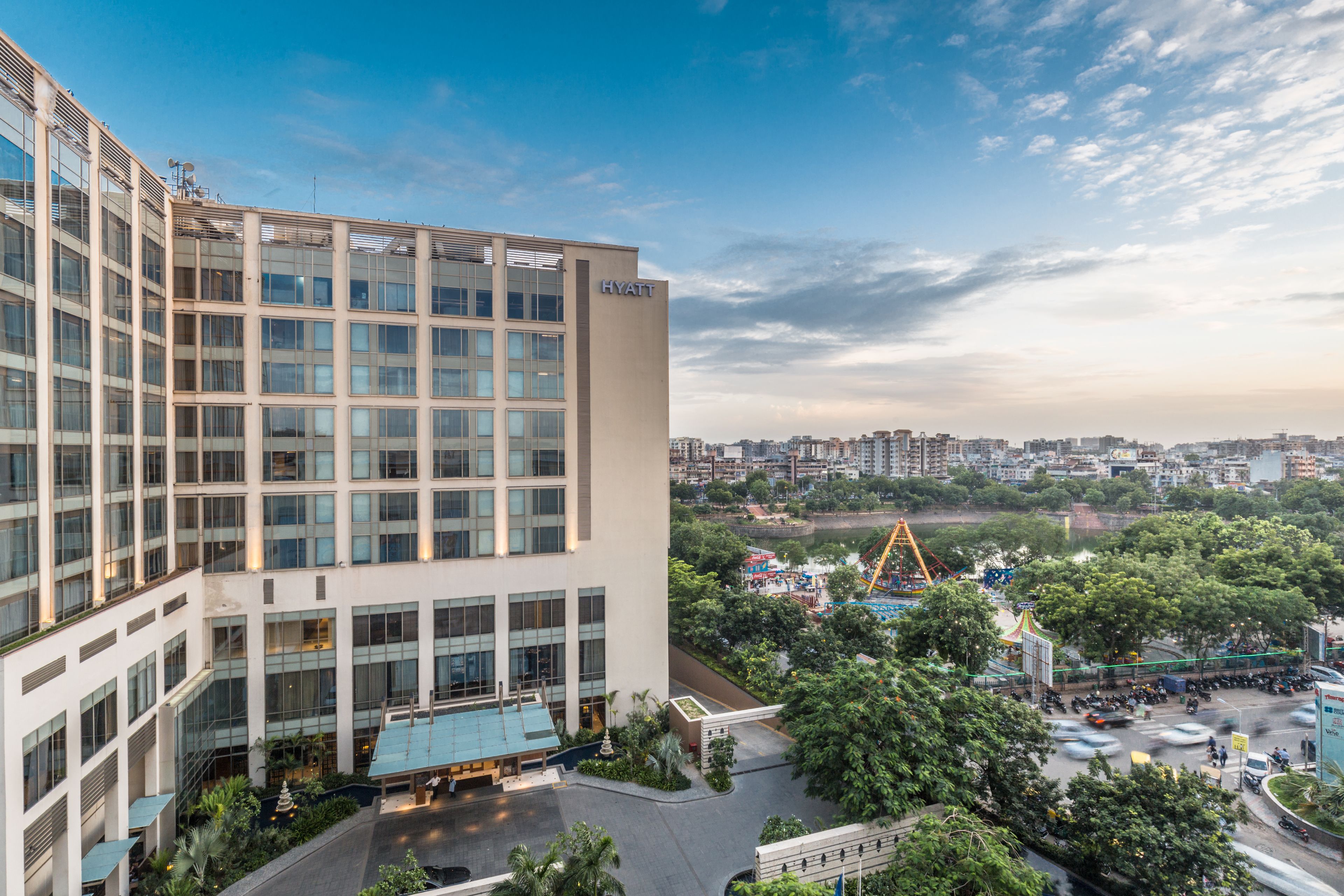 A modern hotel with a glass facade, a rooftop pool, and a view of a nearby amusement park.