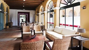 A spacious indoor area with a high ceiling, wicker furniture, a sofa, and a table. - Hotel Isla Canela Golf (Ayamonte)