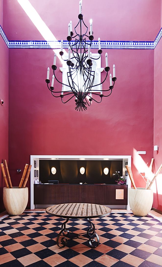 A room with a checkered floor, a dark reception desk, a chandelier, and two wooden planters.