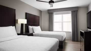 Une chambre d’hôtel avec deux lits, un ventilateur de plafond, une télévision, une table de chevet avec une lampe et une fenêtre avec des rideaux.