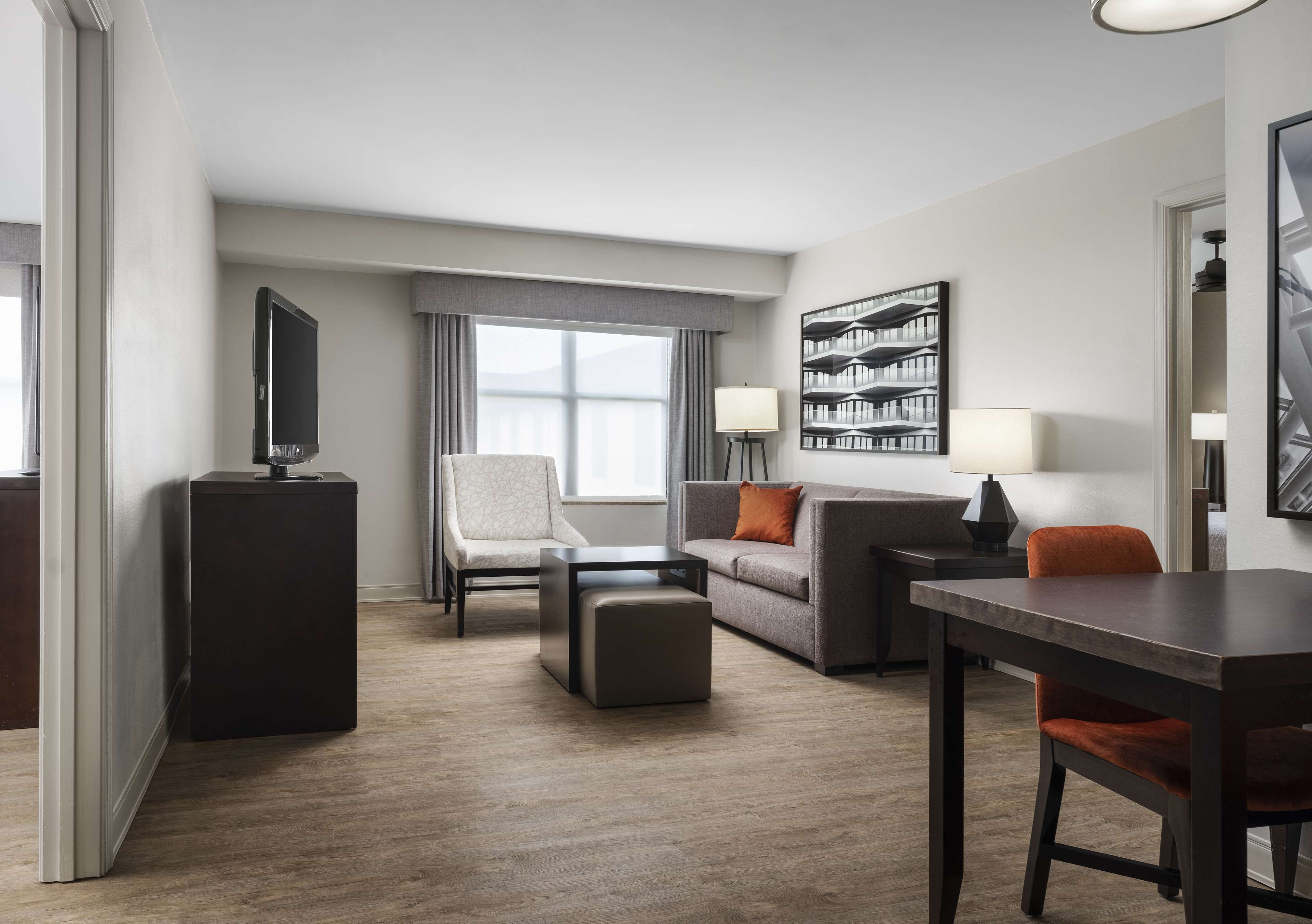 A modern hotel room with a sofa, armchair, ottoman, and a dining table.