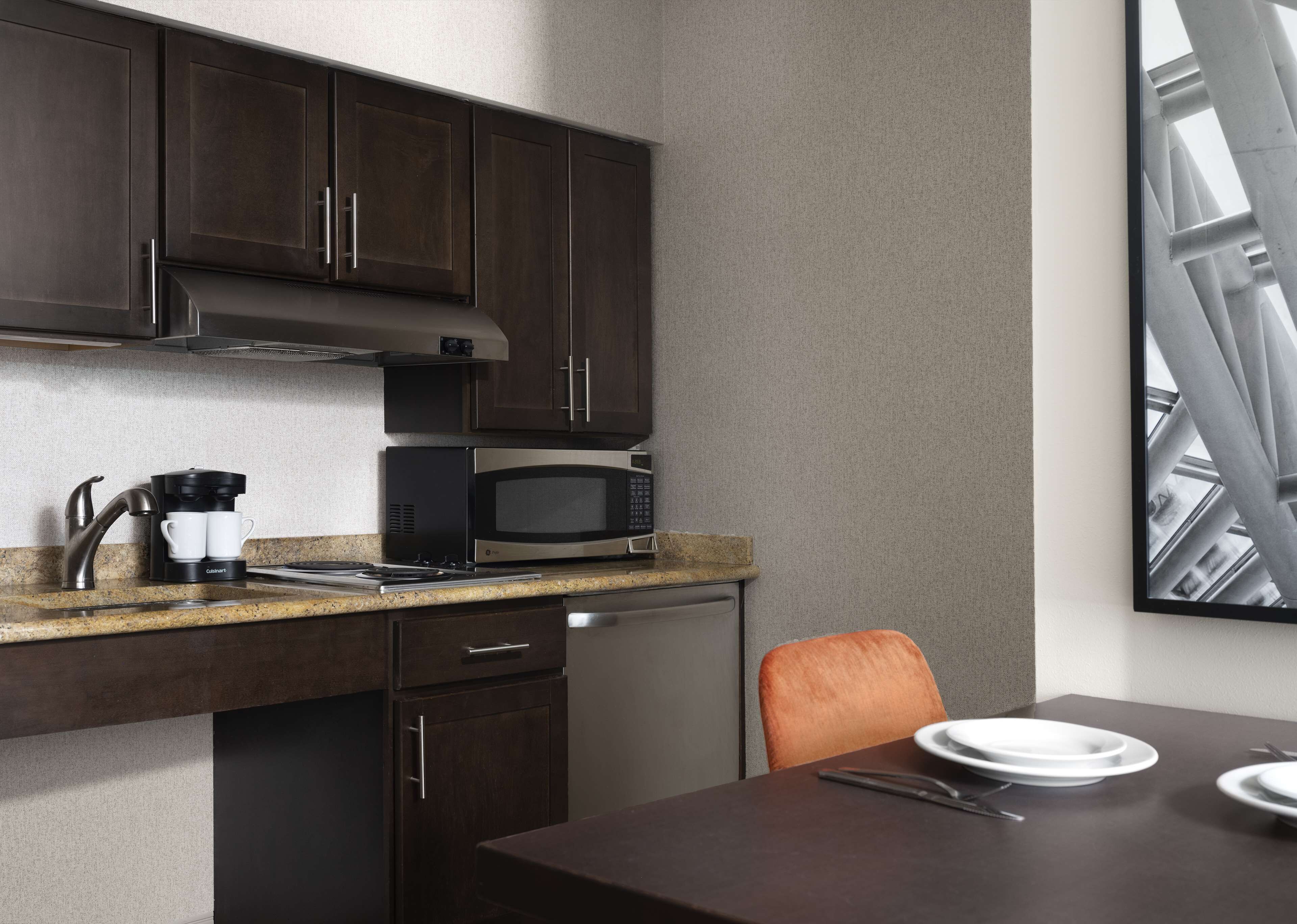 A compact kitchen with dark cabinetry, a microwave, a coffee maker, and a dining area with a table and chairs.