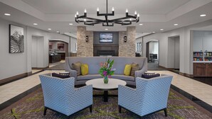A lobby with a grey sofa, two blue armchairs, a round coffee table, and a chandelier. - Homewood Suites by Hilton Carle Place - Garden City, NY (Carle Place)