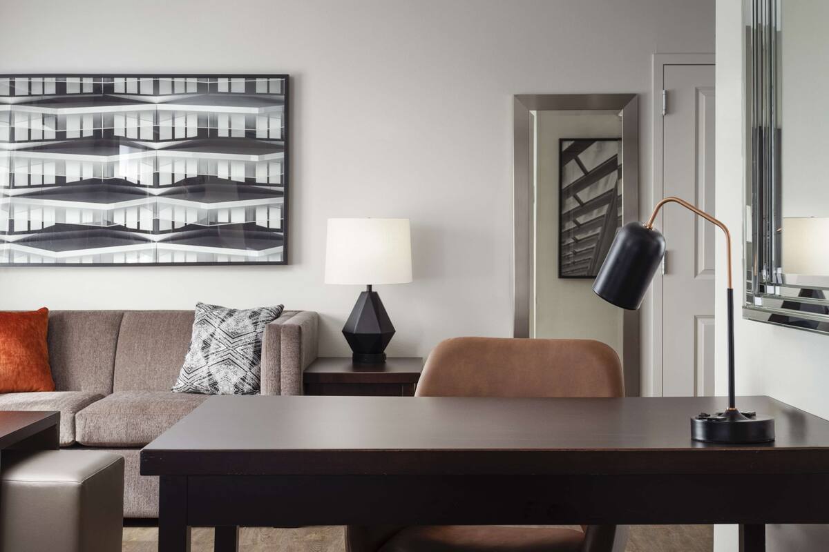 A modern hotel room with a sofa, a table, a lamp, and a large abstract painting on the wall.