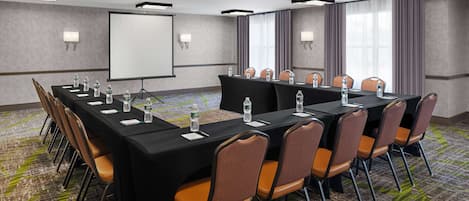 A conference room with a long table, chairs, a projector screen, and a carpeted floor.