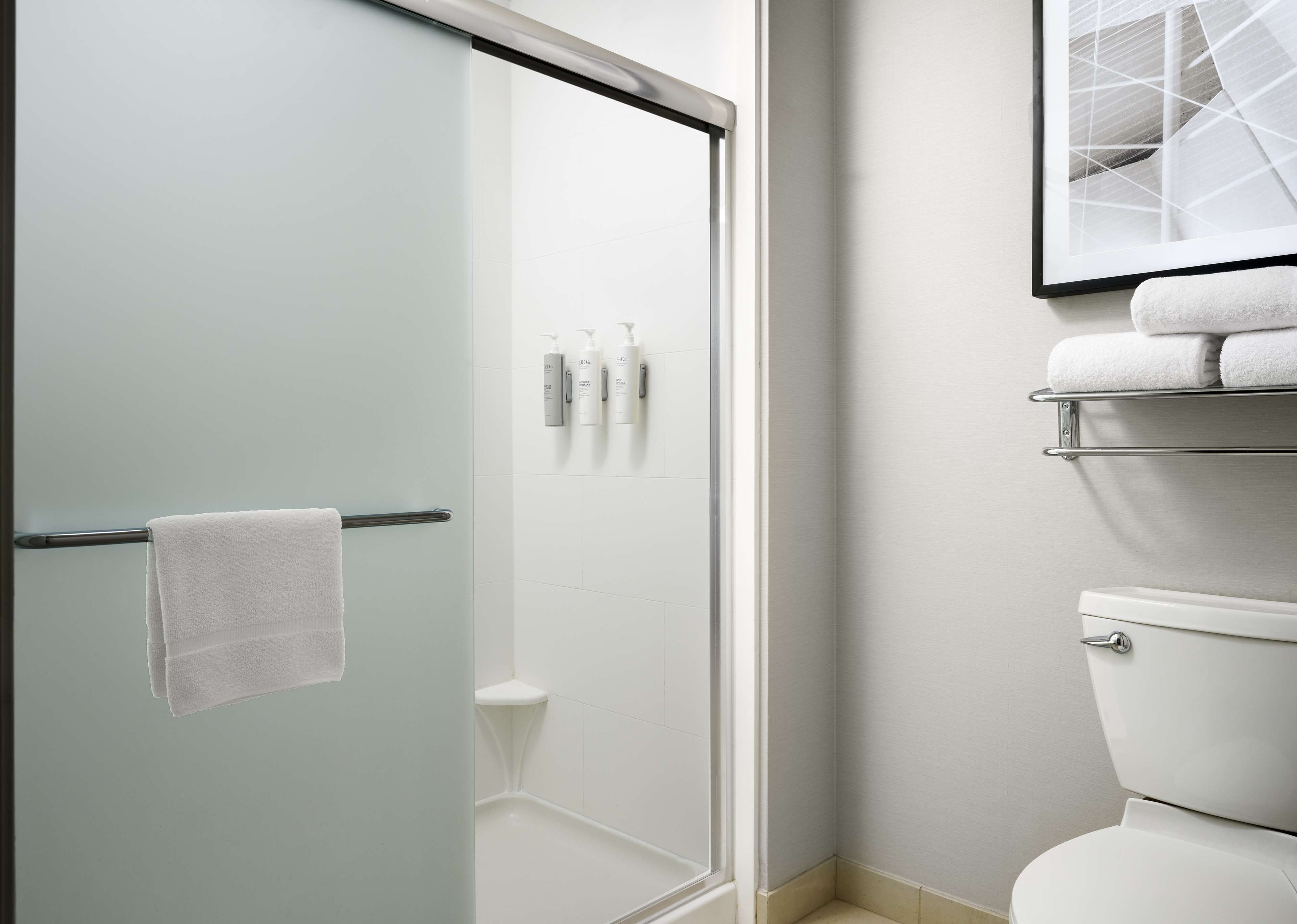 Un baño moderno con mampara de cristal, inodoro y estante con artículos de aseo.