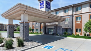 Entrada de un hotel Sleep Inn & Suites con área de estacionamiento techada, pilares de piedra y señalización clara para estacionamiento de discapacitados.