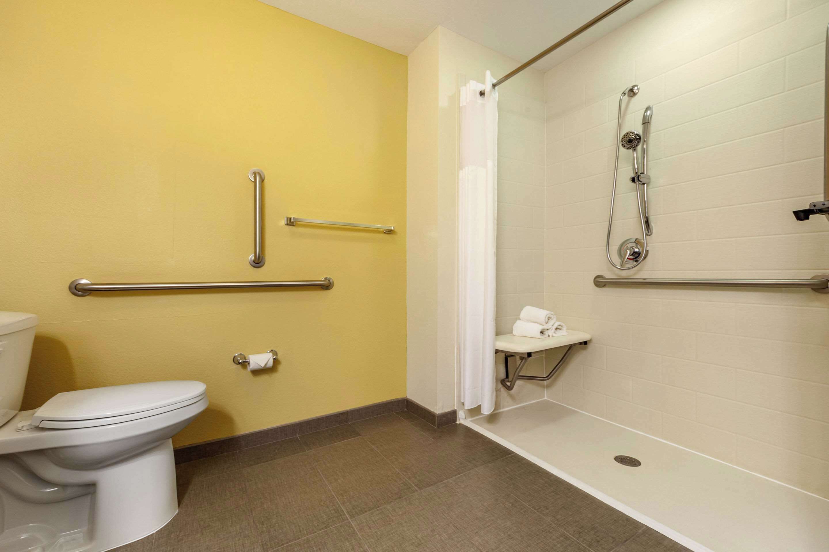 Et badeværelse med toilet, brusebad med gelænder og et gelænder.