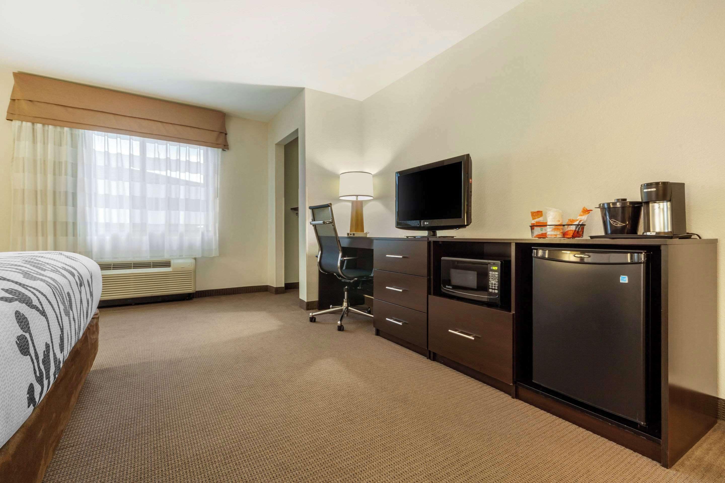 Une chambre d’hôtel équipée d’un lit, d’un bureau avec une télévision, d’un mini-réfrigérateur et d’une machine à café.