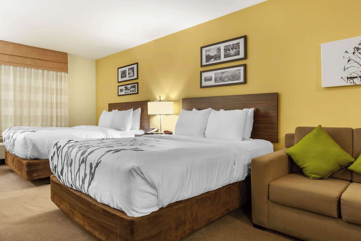 A hotel room with two single beds, a sofa, a lamp, and framed pictures on the wall.