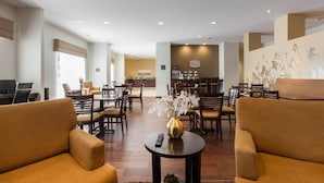 Un hall de hotel con sofás, una mesa de centro con un florero y una zona de comedor al fondo.