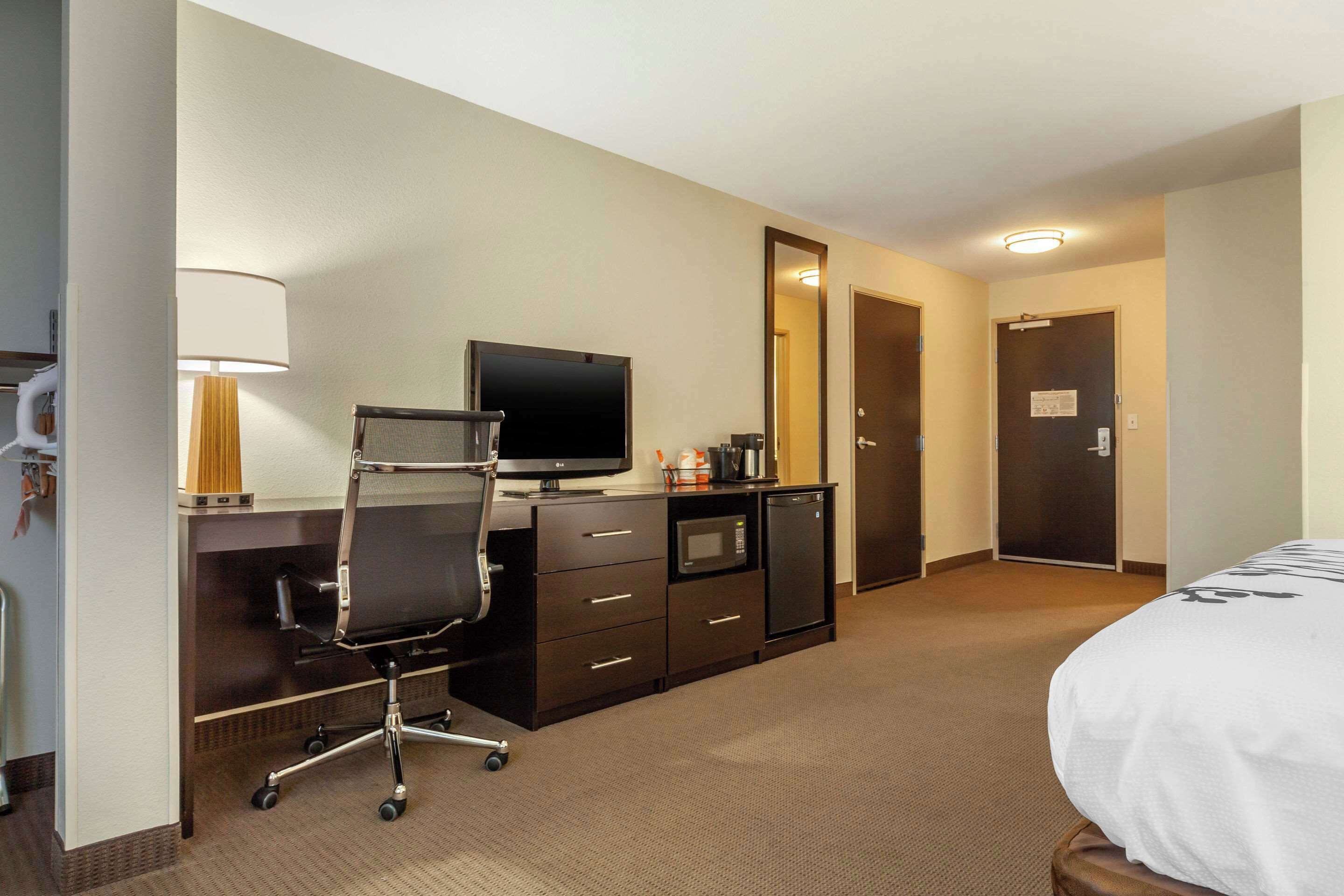 Habitación de hotel con cama, escritorio con computadora, silla, televisor, microondas y refrigerador pequeño.