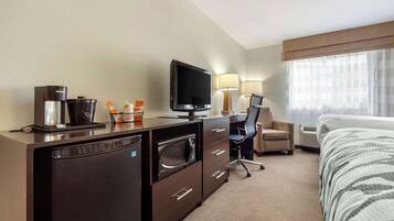 A hotel room with a bed, a desk with a coffee maker, a television, a chair, and a lamp.