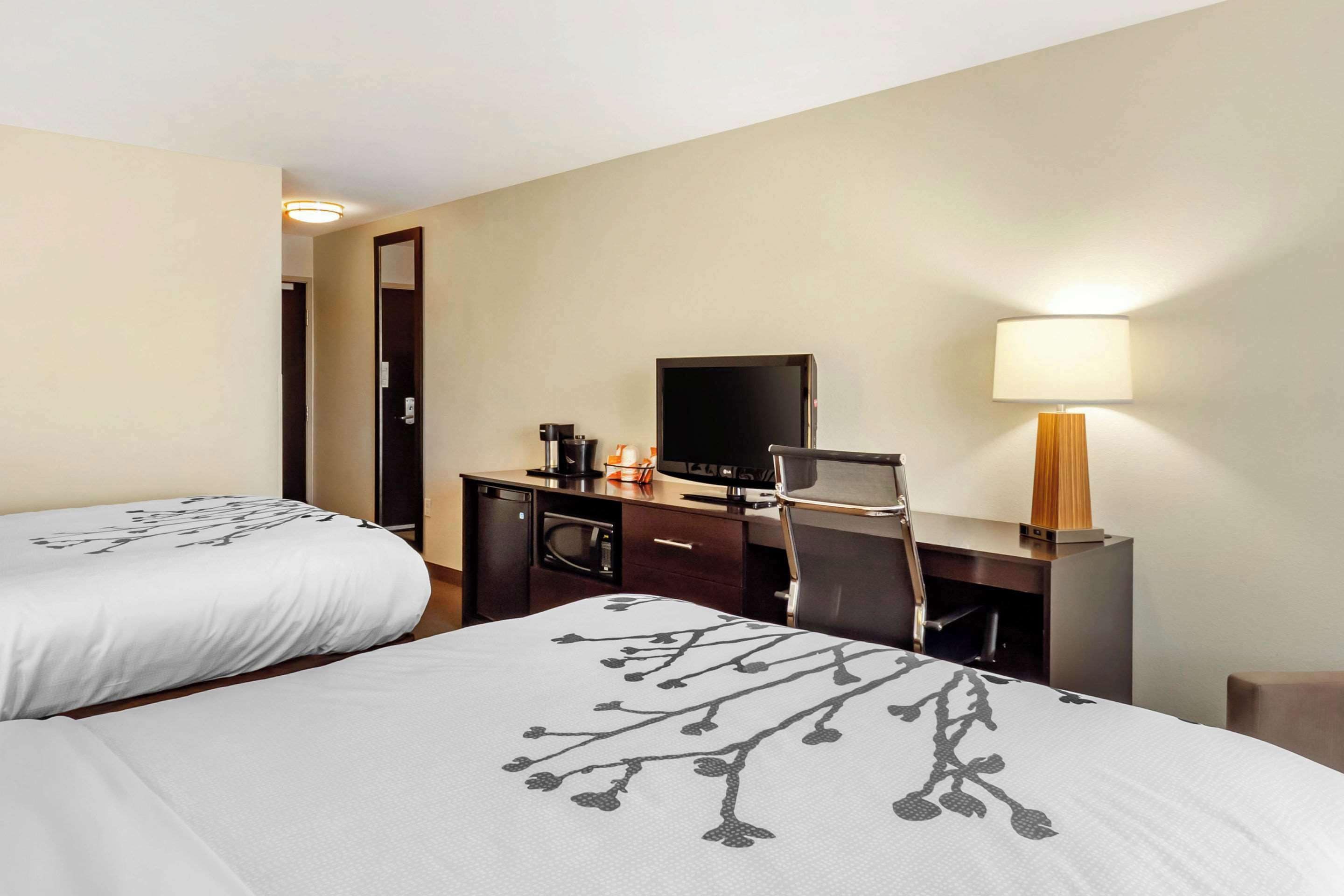 A hotel room with two beds, a desk with a computer, a coffee maker, and a lamp.