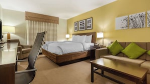 Habitación de hotel con cama, escritorio, silla, sofá y mesa de centro. Hay tres cuadros enmarcados en la pared.